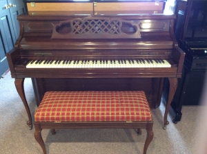 brown piano with bench with red and gold cover