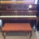 brown piano with bench with red and gold cover