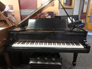 black grand piano with lid and key cover open and bench in front