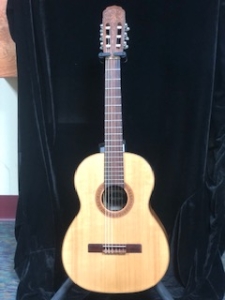 nylon string giannini guitar on stand in front of black background