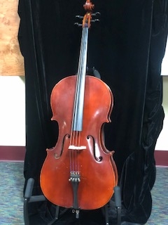 brown cello on stand in front of black background