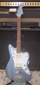 Used Fender Ventera Jazzmaster Guitar in Ice Blue Metallic sitting on a guitar stand in front of an amp.