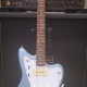 Used Fender Ventera Jazzmaster Guitar in Ice Blue Metallic sitting on a guitar stand in front of an amp.