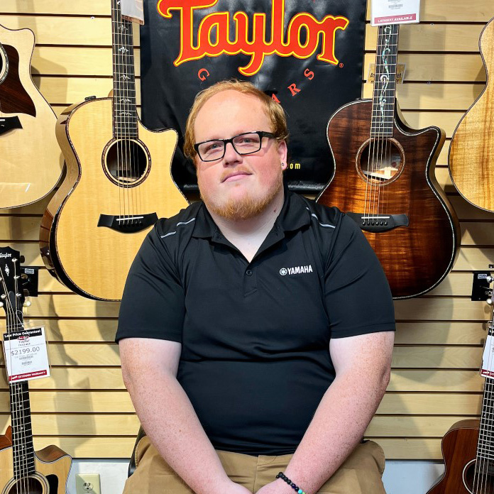 Karl Chugg, Manaager of the Florence Store sitting in front of guitars.